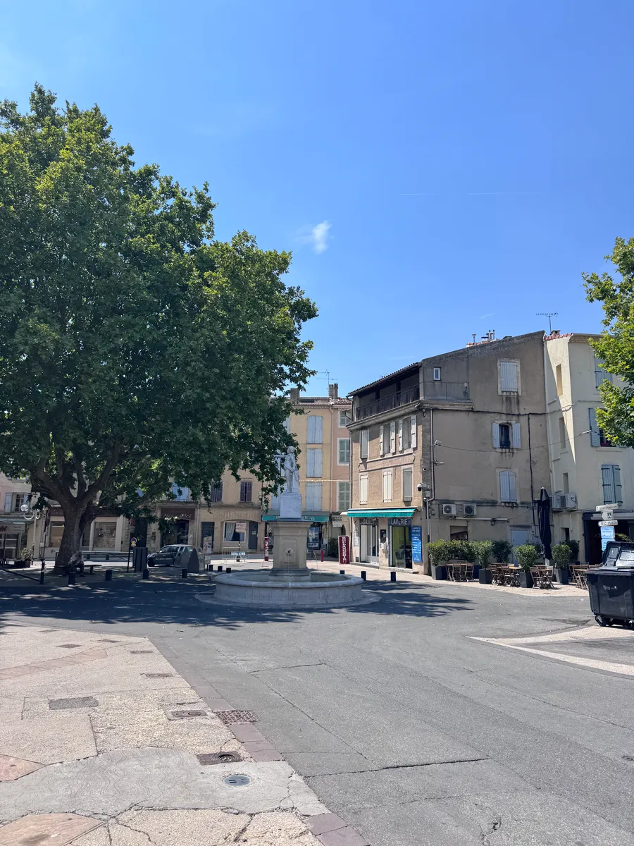Place de village à Pertuis : la fontaine et les terrasses à l'ombre d'un grand platane, un matin d'été